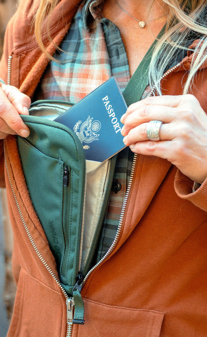 A person places their passport inside of a green travel neck wallet.