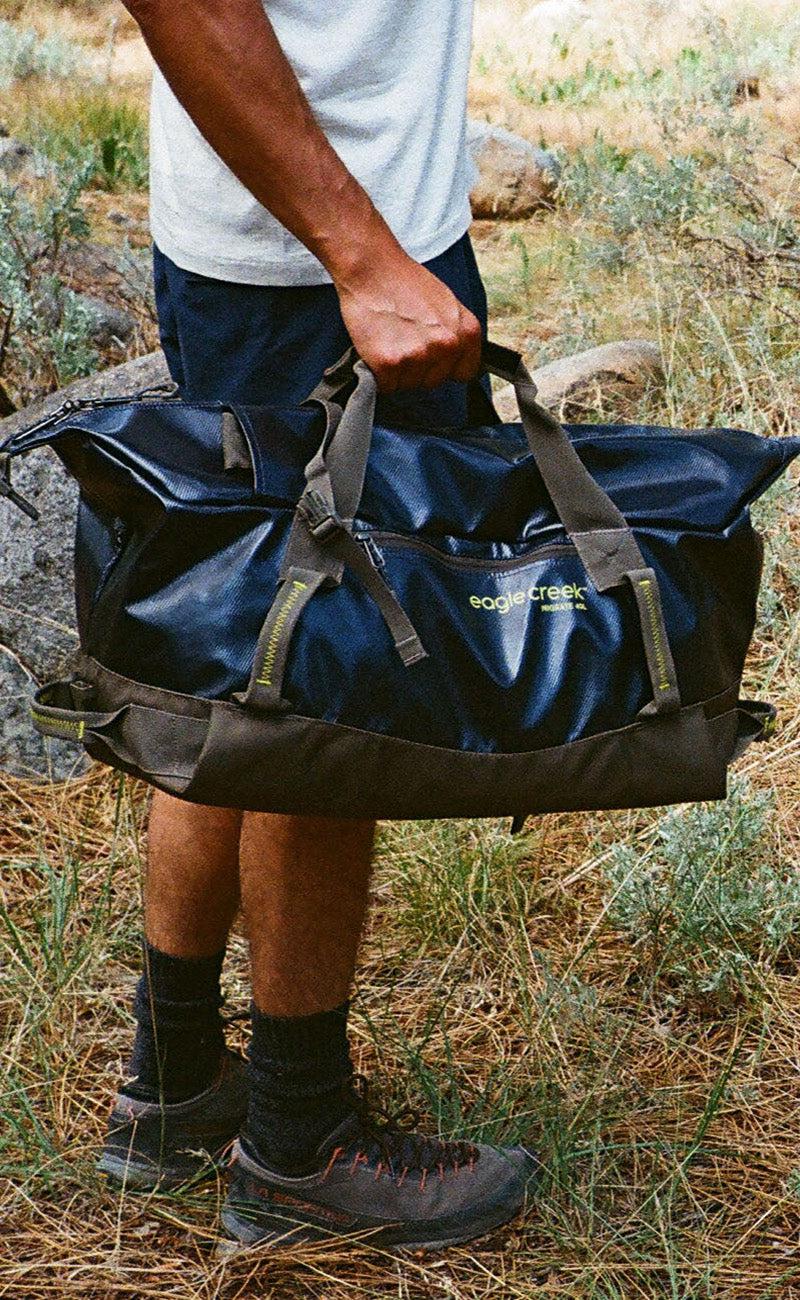 A person holding a blue waterproof duffle bag by their side.