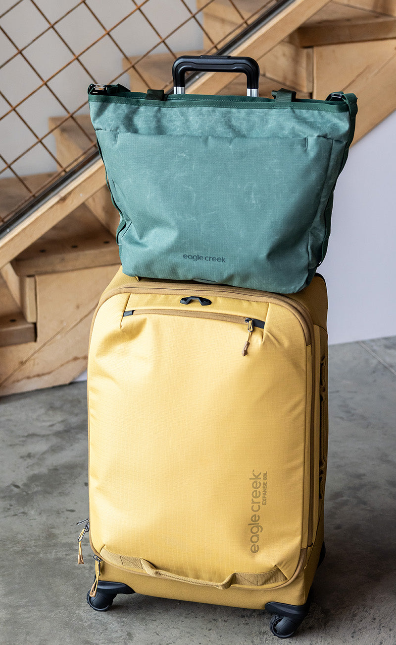 A green travel tote bag sits on top of a piece of yellow rolling luggage.