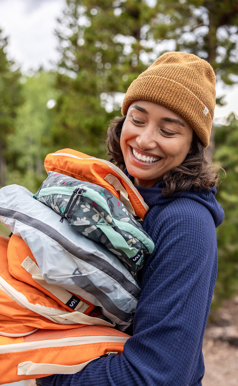 A person smiles while holding a stack of orange and white packing cubes.